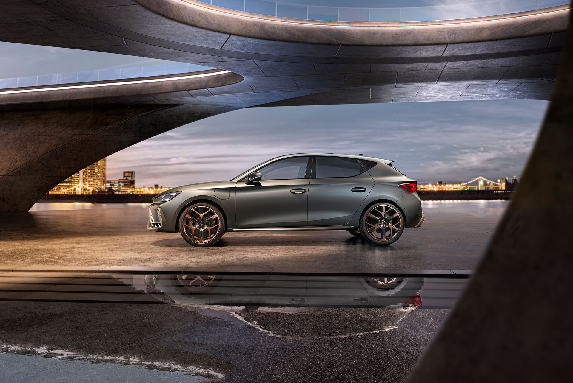 wide shot of new cupra leon 2024 side view in grey parked on smooth concrete under architectural structure with view of the sea and cityscape, cloudy sky. 