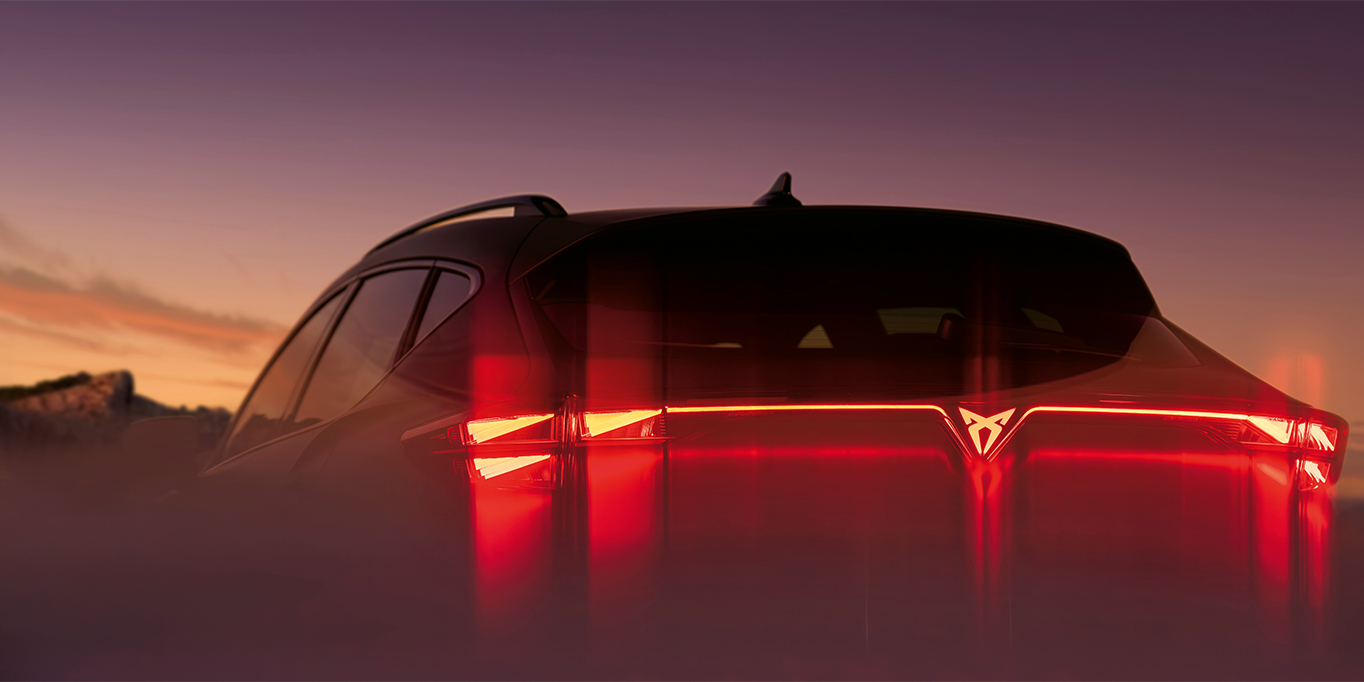 Rear view of the CUPRA Formentor with illuminated rear lights at night, set against a dramatic landscape.