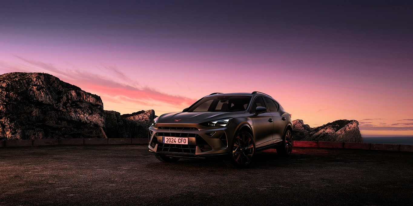 A three-quarter view of the new CUPRA Formentor 2024 parked on gravel at dusk, featuring a sleek, metallic body against a backdrop of rugged cliffs and ethereal sunset.