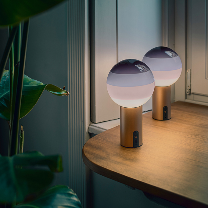 two cupra x marset dipping lights with spherical frosted glass tops and purple gradients are lit, creating a warm, ambient light. The portable lamps’ metallic copper bases both have a switch.