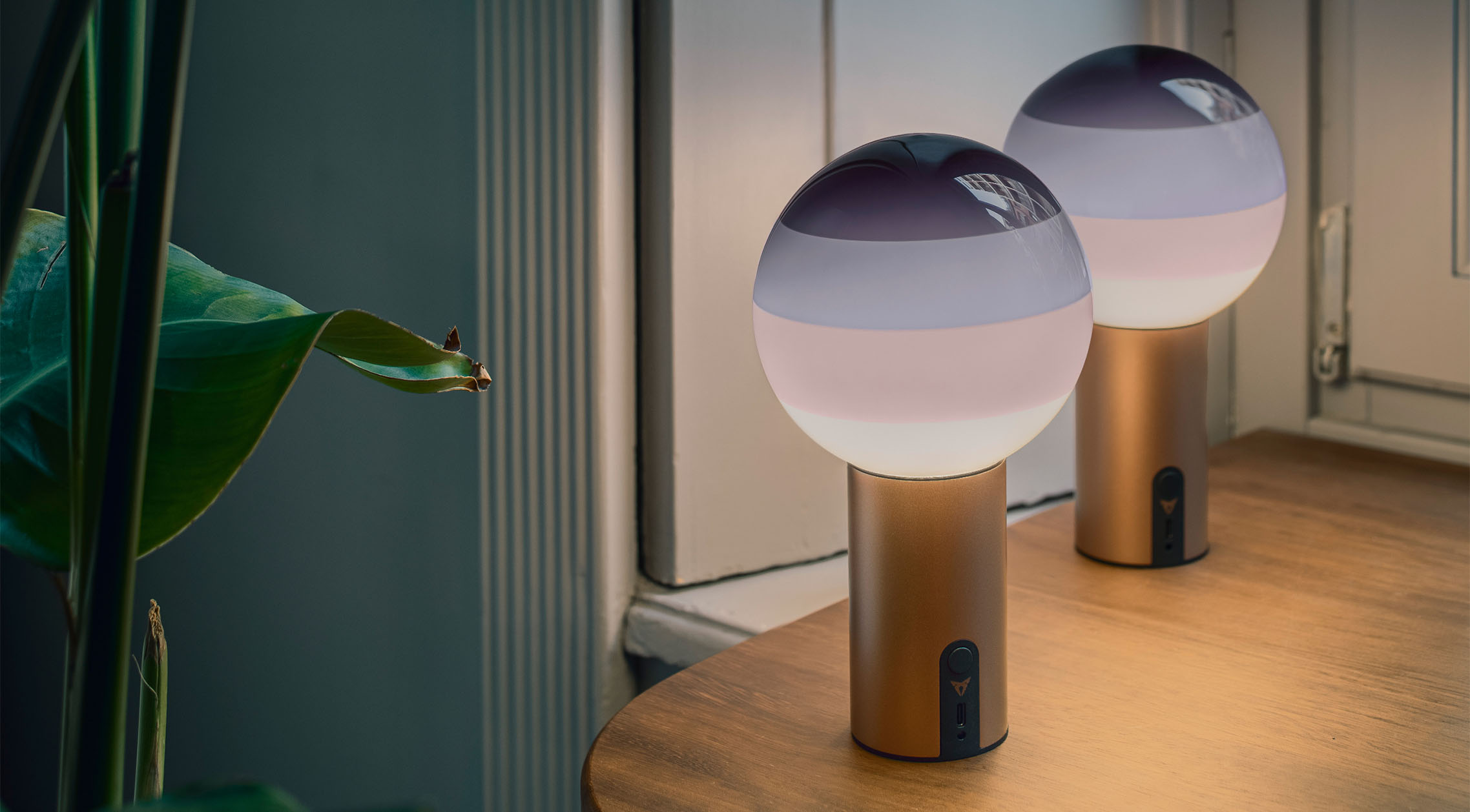  two cupra x marset dipping lights with spherical frosted glass tops and purple gradients are lit, creating a warm, ambient light. The portable lamps’ metallic copper bases both have a switch.