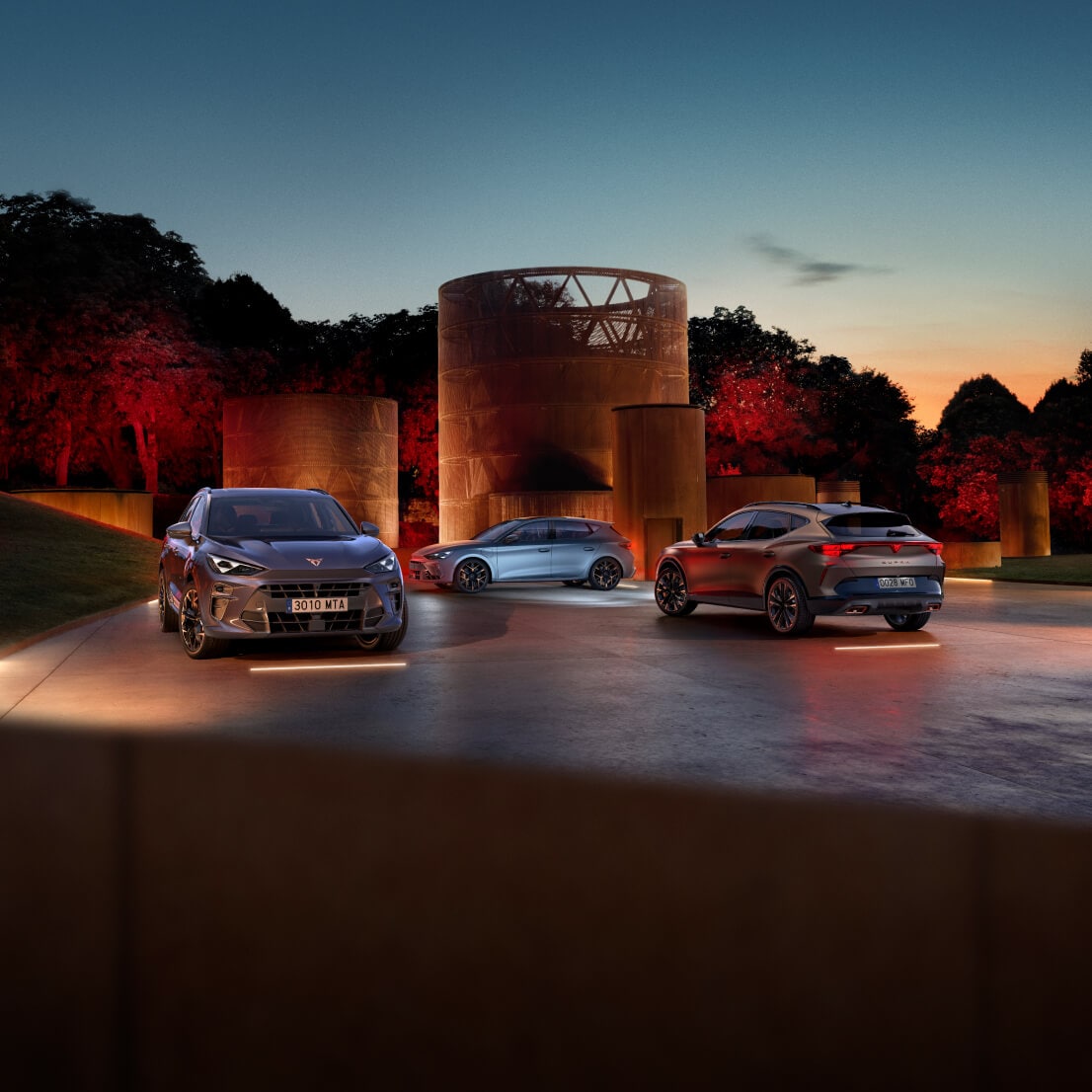 Cupra born, cupra leon sportstourer, and cupra formentor parked at dusk in a modern outdoor setting with a cylindrical building and red lit trees in the background.