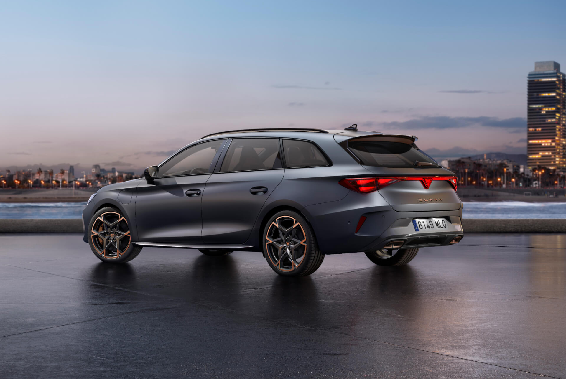 The sporty new 2024 Cupra Leon Sportstourer parked on concrete with a city skyline illuminated at twilight in the background. The vehicle is depicted in a matte grey finish.