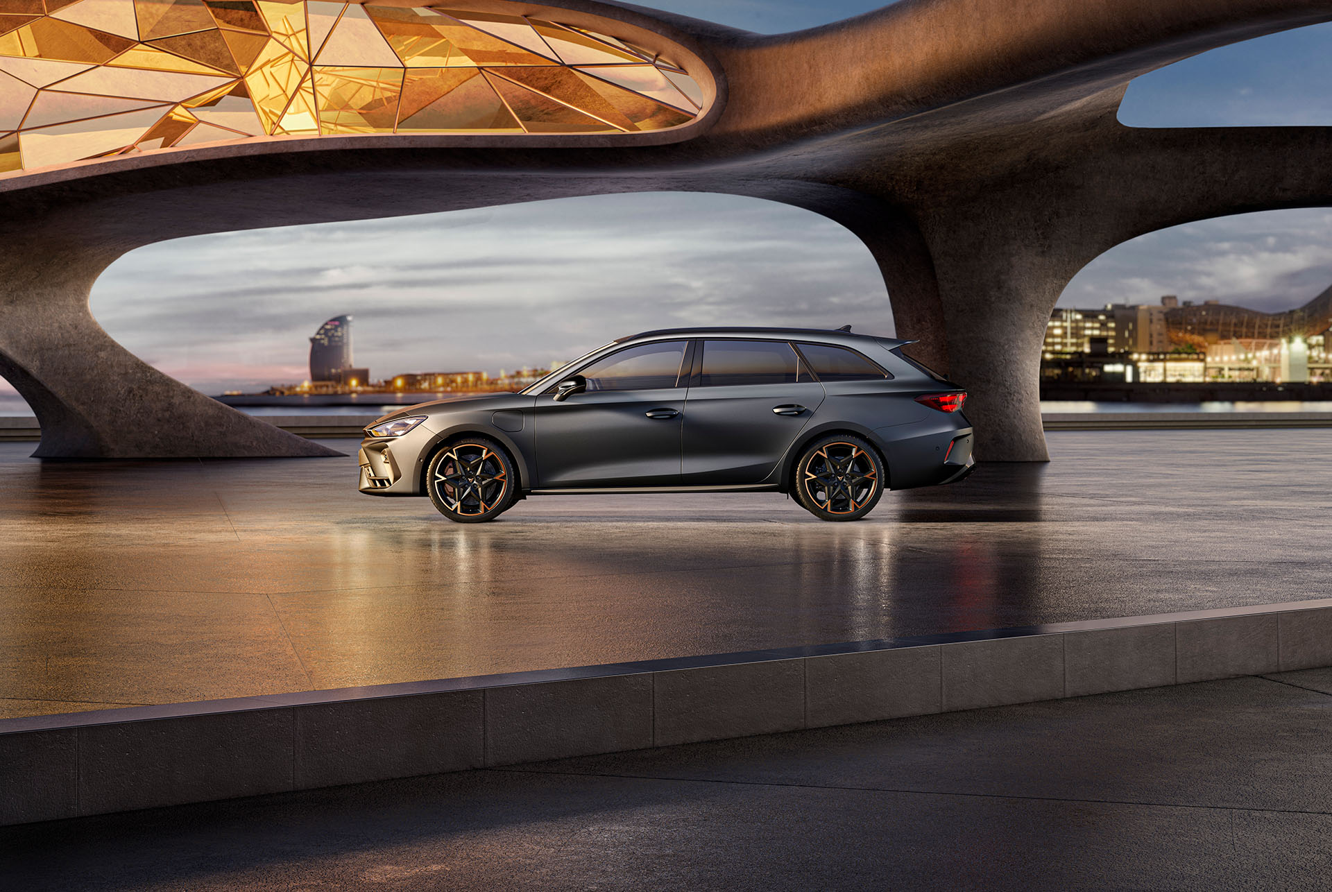 New cupra leon sportstourer 2024 cars and equipment parked on cement, structure with glowing edges, overlooking a city skyline at dusk. The vehicle is shown in a matte grey finish with copper and black alloy wheels.