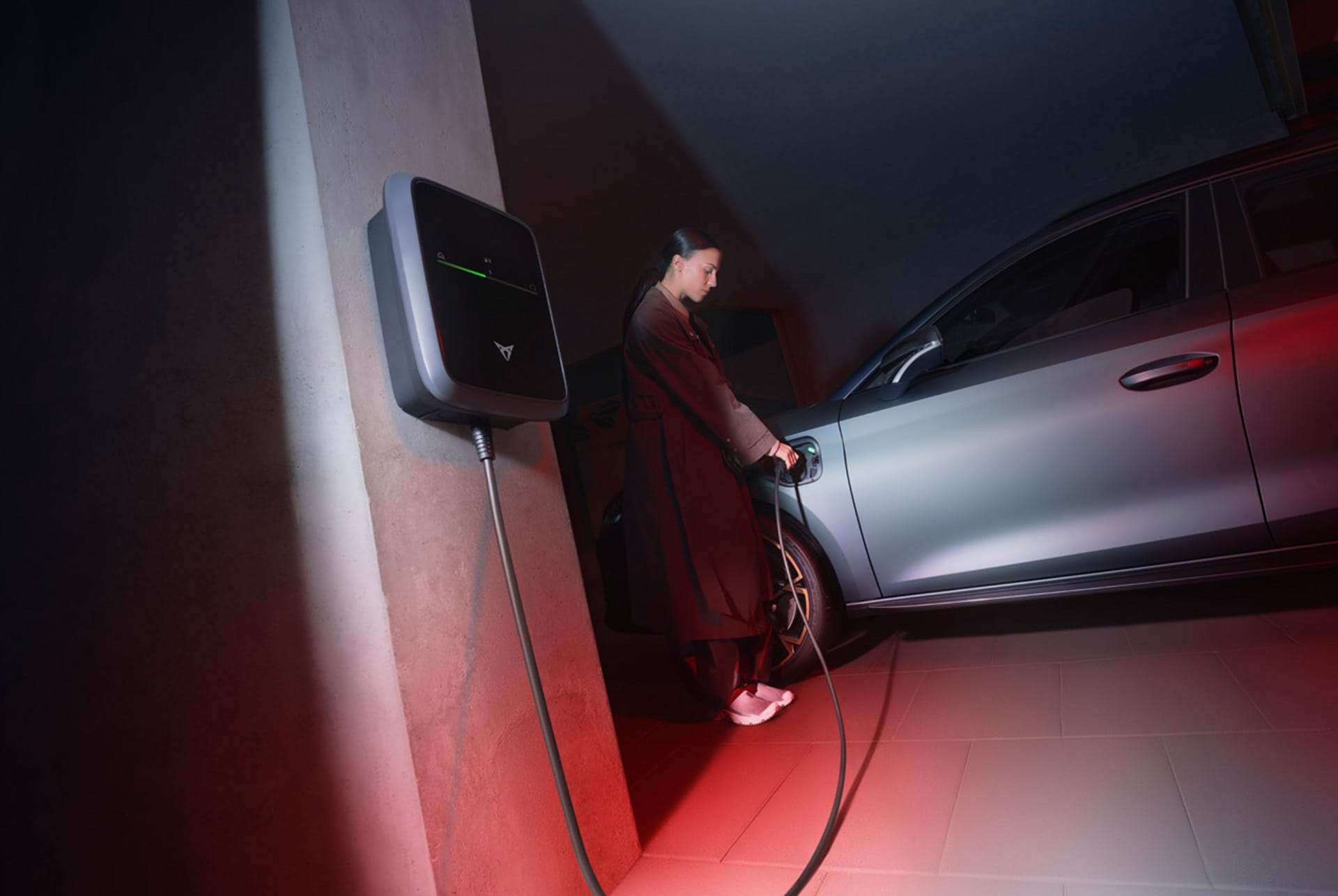 front side view of the new Cupra Leon Sportstourer 2024 hybrid vehicle in matte grey which is being plugged in by a woman with a charging cable.