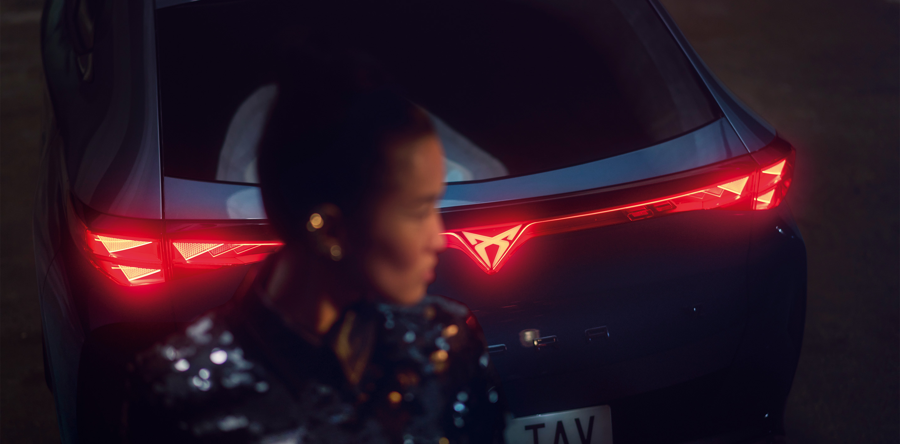 rear view of cupra tavascan at night with a person standing nearby, representing cupra customer support