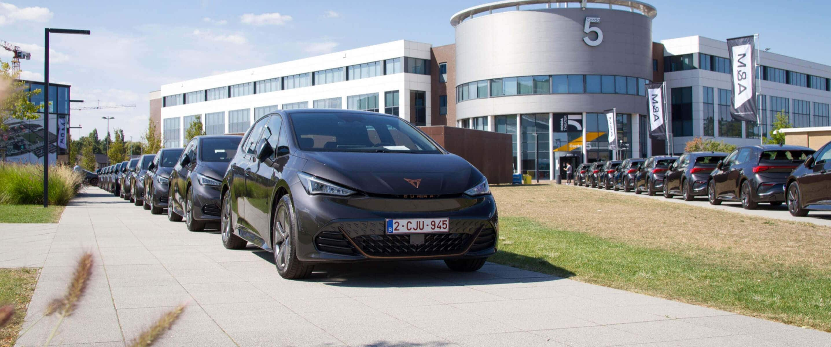 A row of cupra born cars with cegeka branding parked in a line outside a modern office building on a sunny day.