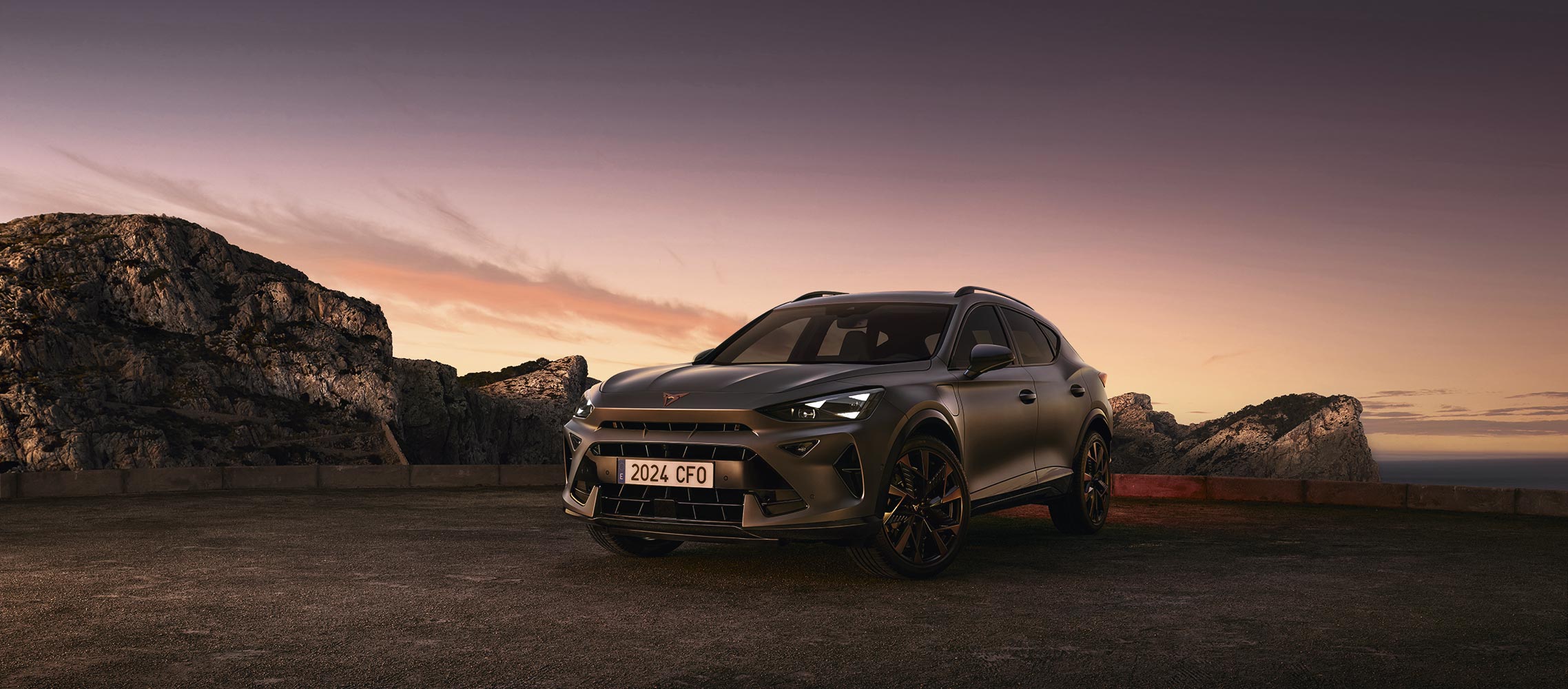 cupra formentor plug-in hybrid electric vehicle parked on gravel at dusk, featuring a sleek, metallic body against a backdrop of rugged cliffs and ethereal sunset